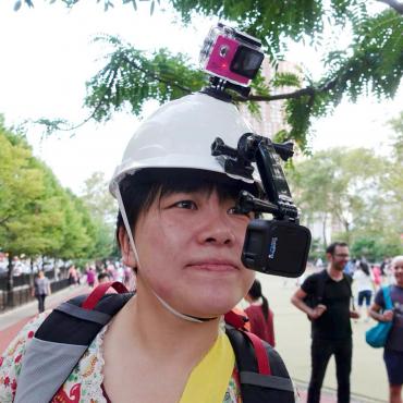 Ying Liu, an Asian woman wearing a white hard hat mounted with two GoPro Cameras, looks on.